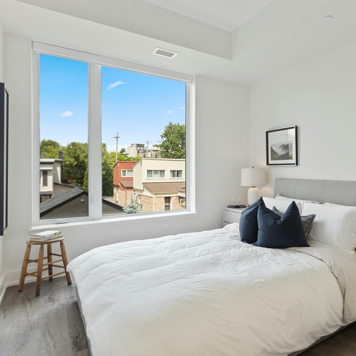 Helles Schlafzimmer mit weißer Bettwäsche, dunkelblauen Kissen und großem Fenster