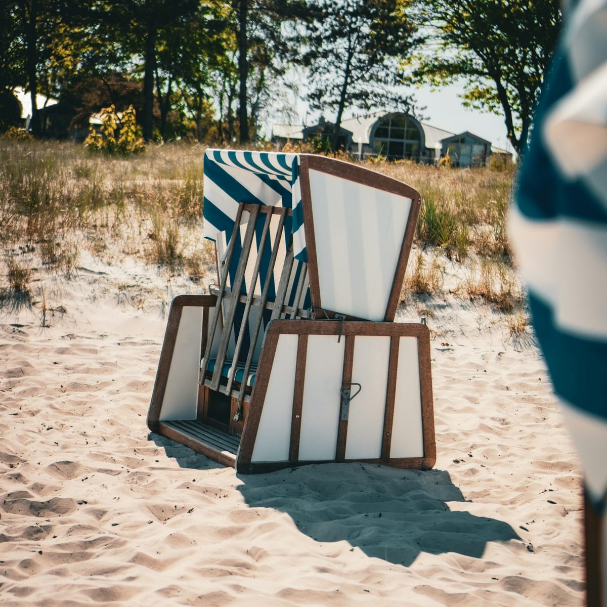 Blau-weiß gestreifter Strandkorb im Sand zwischen Dünengras