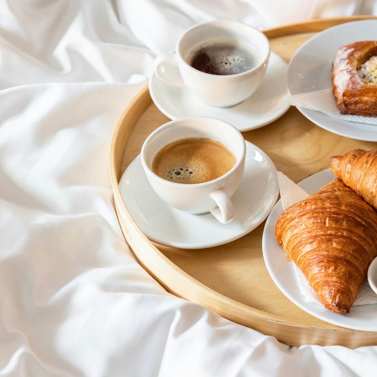Frühstückstablett mit Kaffee und Croissants auf weißer Bettwäsche